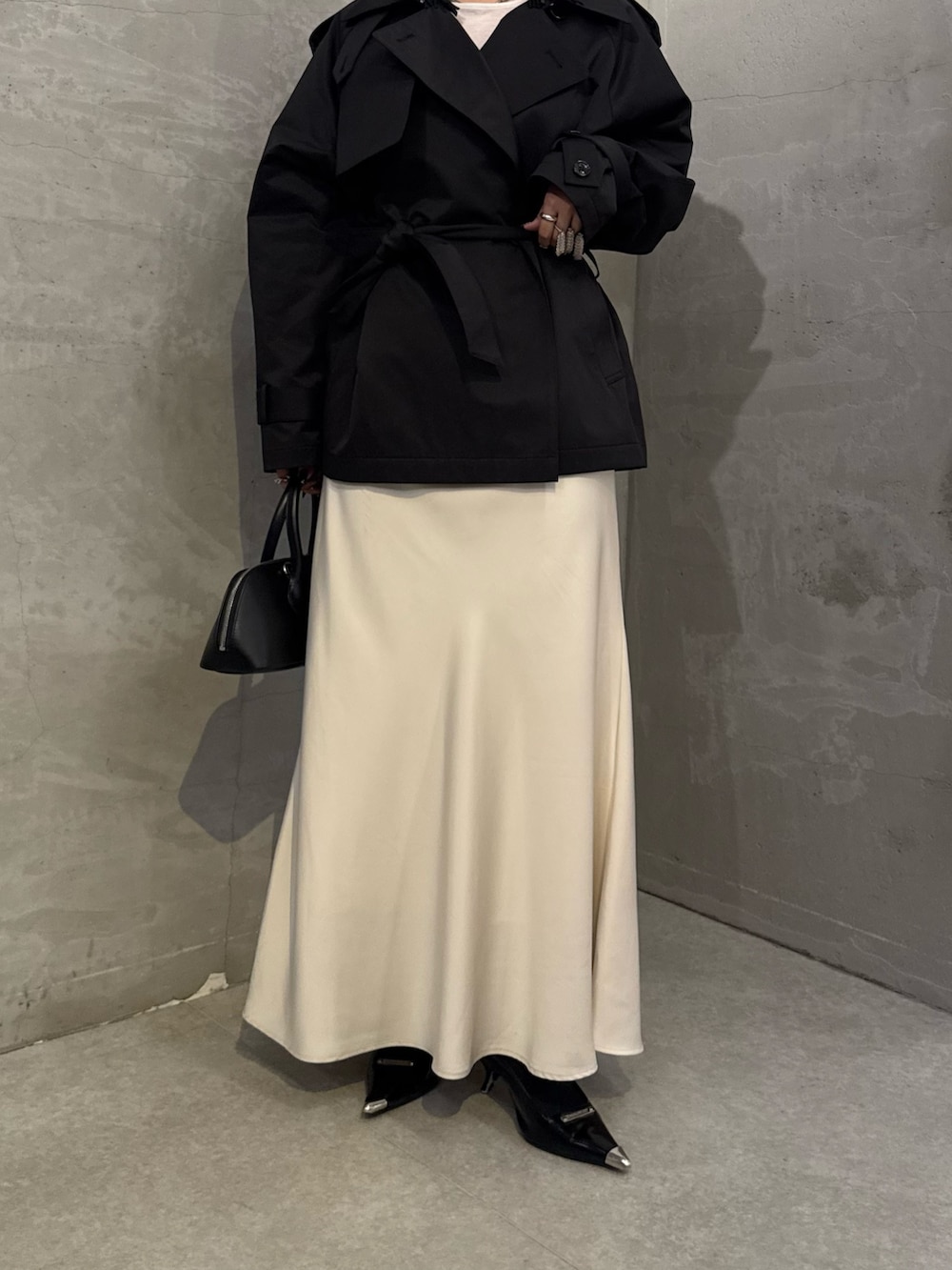 ブラック系のトレンチコート、ホワイト系のスカート、ブラック系のショルダーバッグを着用したレディースの冬コーディネートの6枚目の写真