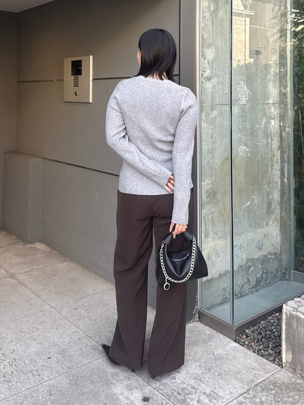 グレー系のニット/セーター、ブラウン系のスラックス、ブラック系のトートバッグを着用したレディースの冬コーディネートの2枚目の写真