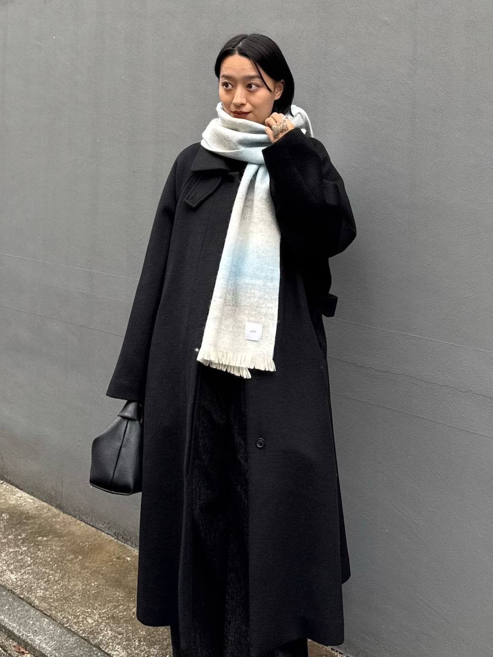 ブラック系のチェスターコート、ブラック系のトートバッグ、ブラック系のデニムパンツを着用したレディースの秋コーディネートの3枚目の写真
