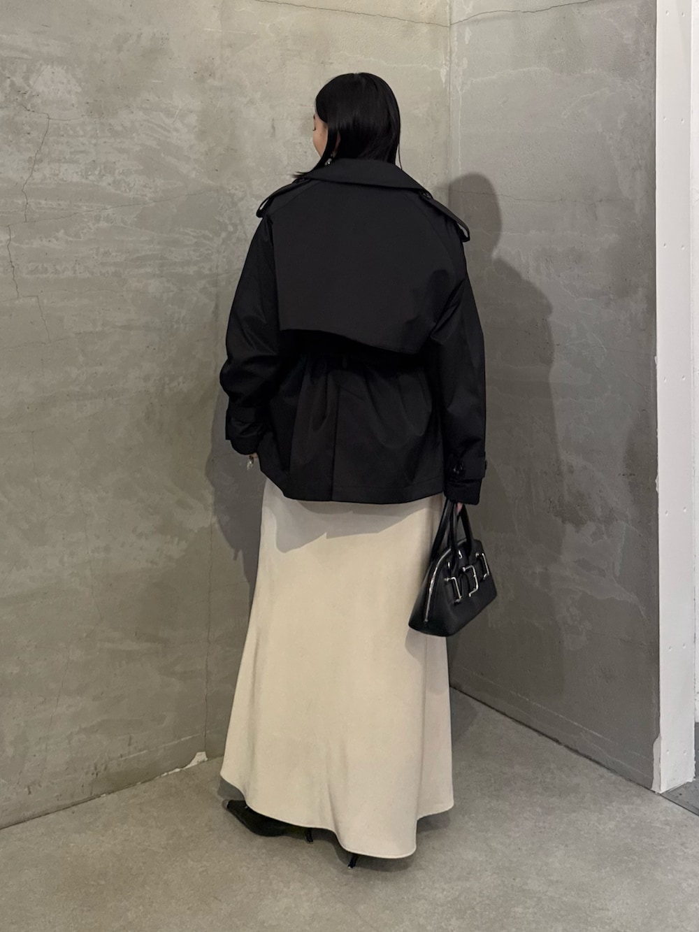 ブラック系のトレンチコート、ホワイト系のスカート、ブラック系のショルダーバッグを着用したレディースの冬コーディネートの3枚目の写真