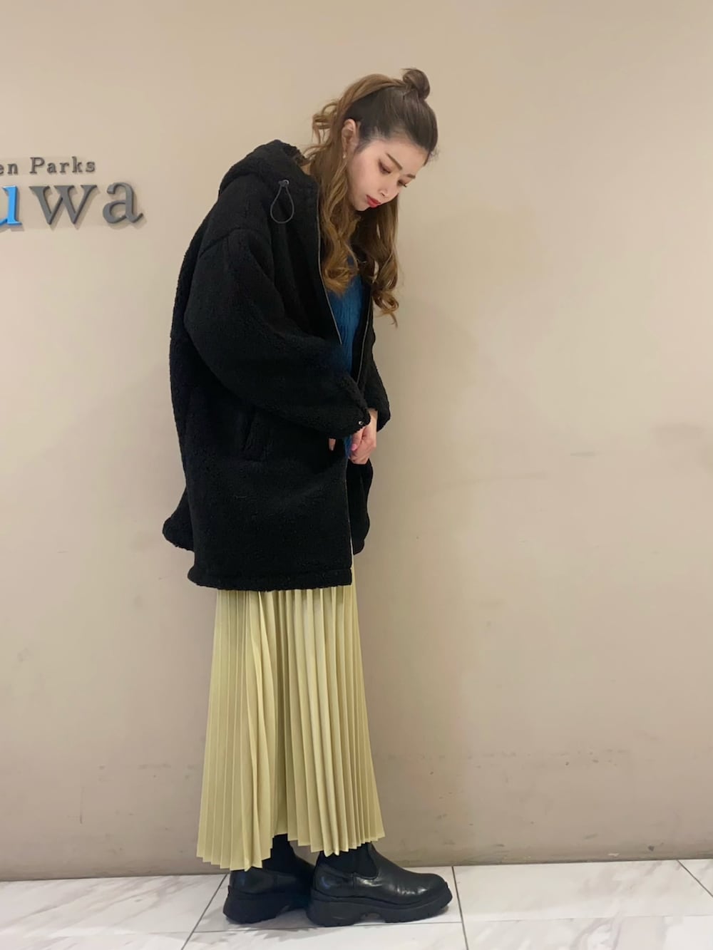 ブラック系のブーツ、イエロー系のスカート、ブラック系のその他アウターを着用したレディースの冬コーディネートの2枚目の写真