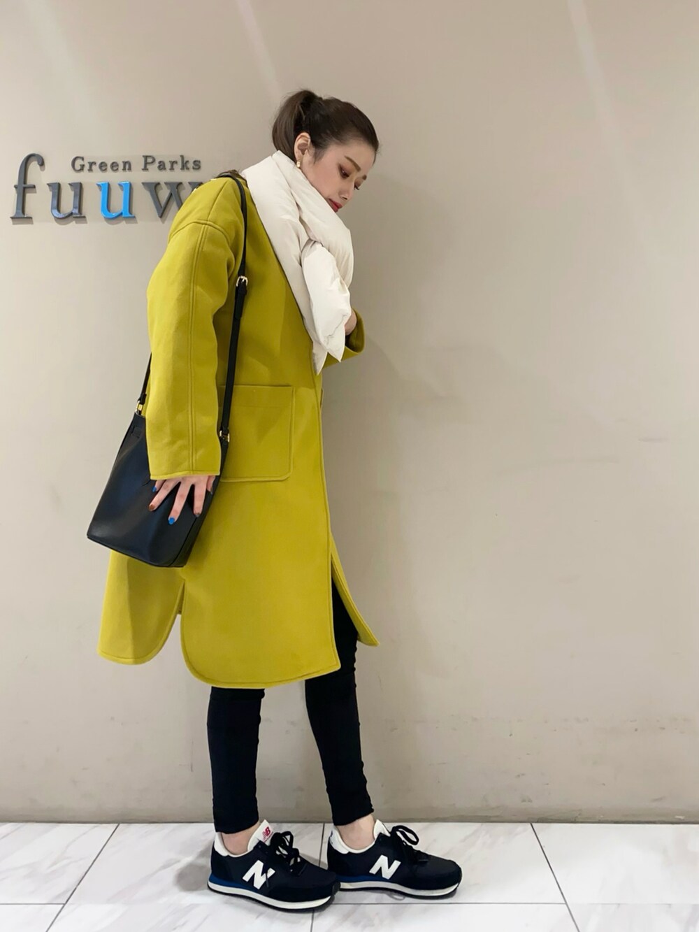 イエロー系のノーカラーコート、ブラック系のショルダーバッグ、ブラック系のパンツを着用したレディースの冬コーディネートの2枚目の写真