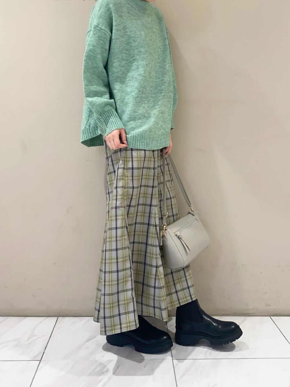 ブルー系のスカート、グリーン系のニット/セーター、ブラック系のブーツを着用したレディースの秋コーディネートの2枚目の写真