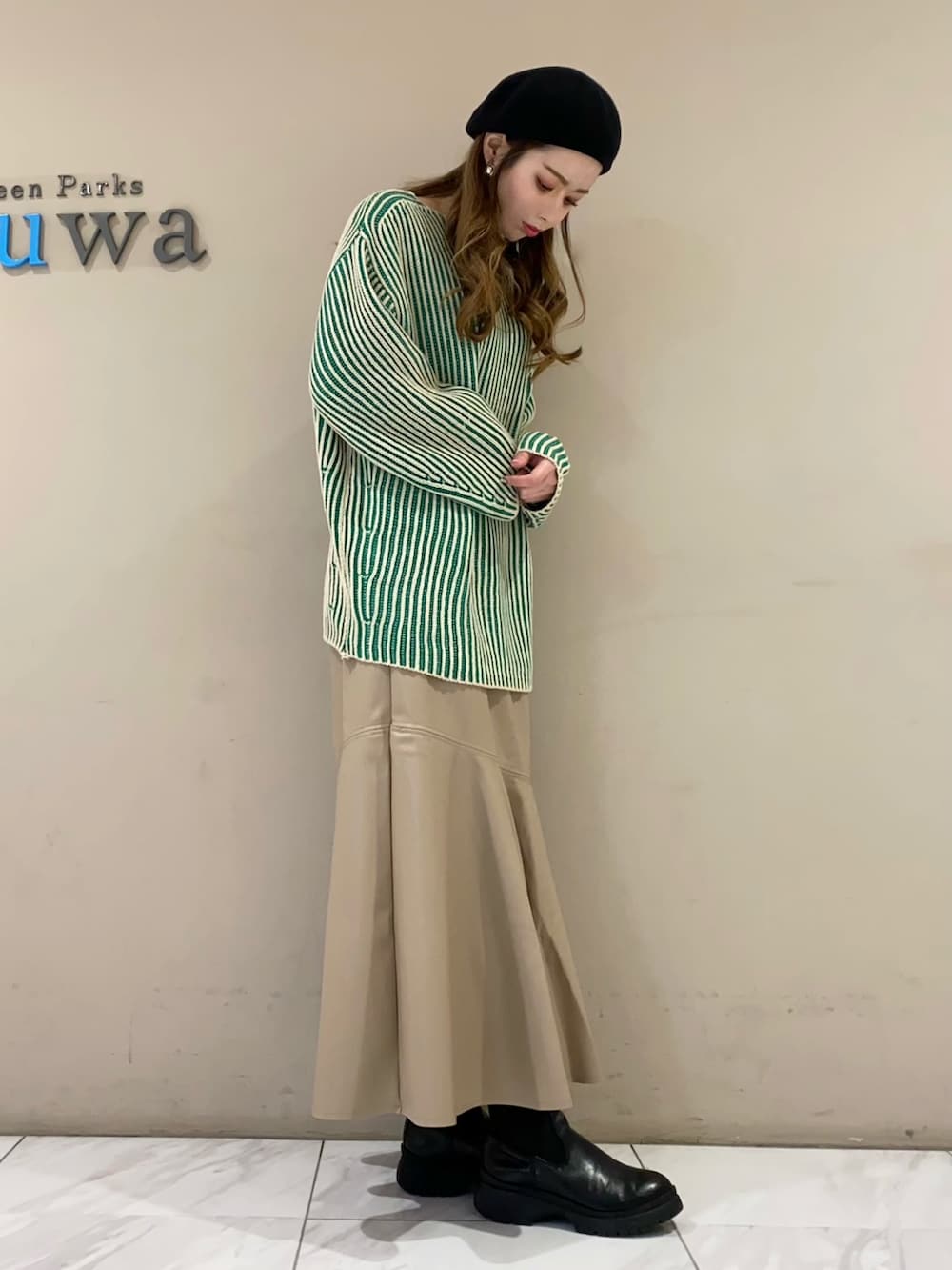 グリーン系のニット/セーター、ベージュ系のスカート、ブラック系のブーツを着用したレディースの冬コーディネートの2枚目の写真