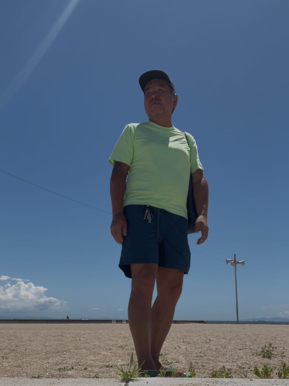 グリーン系のTシャツ/カットソー、グリーン系のサンダル、ブルー系のエコバッグ/サブバッグを着用したメンズの夏コーディネートの3枚目の写真