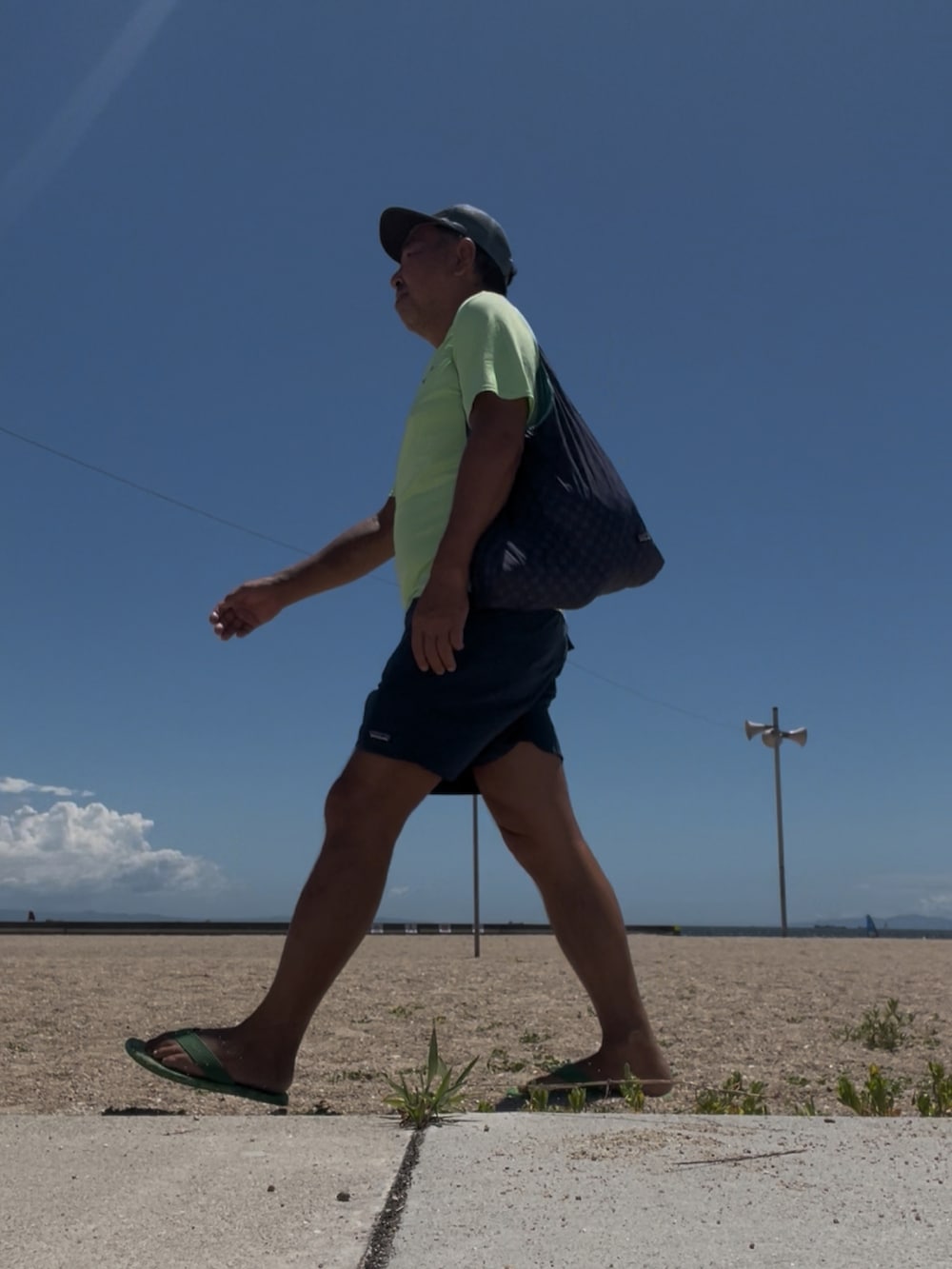 グリーン系のTシャツ/カットソー、グリーン系のサンダル、ブルー系のエコバッグ/サブバッグを着用したメンズの夏コーディネートの2枚目の写真