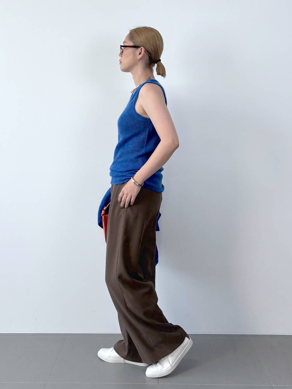 オレンジ系のハンドバッグ、ホワイト系のスニーカー、ブルー系のニット/セーターを着用したレディースの夏コーディネートの5枚目の写真