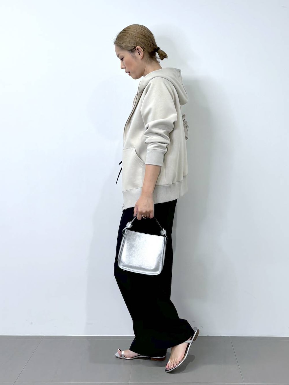 シルバー系のハンドバッグ、ベージュ系のパーカー、シルバー系のサンダルを着用したレディースの夏コーディネートの2枚目の写真