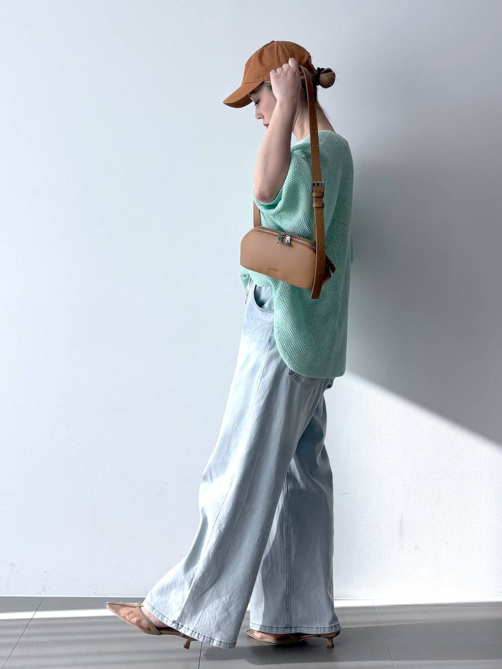 ブルー系のデニムパンツ、グリーン系のニット/セーター、ブラウン系のショルダーバッグを着用したレディースの春コーディネートの3枚目の写真