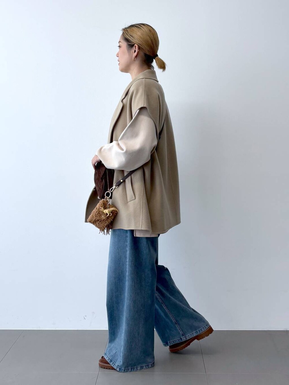 ブルー系のデニムパンツ、ベージュ系のベスト、ブラウン系のショルダーバッグを着用したレディースの秋コーディネートの3枚目の写真