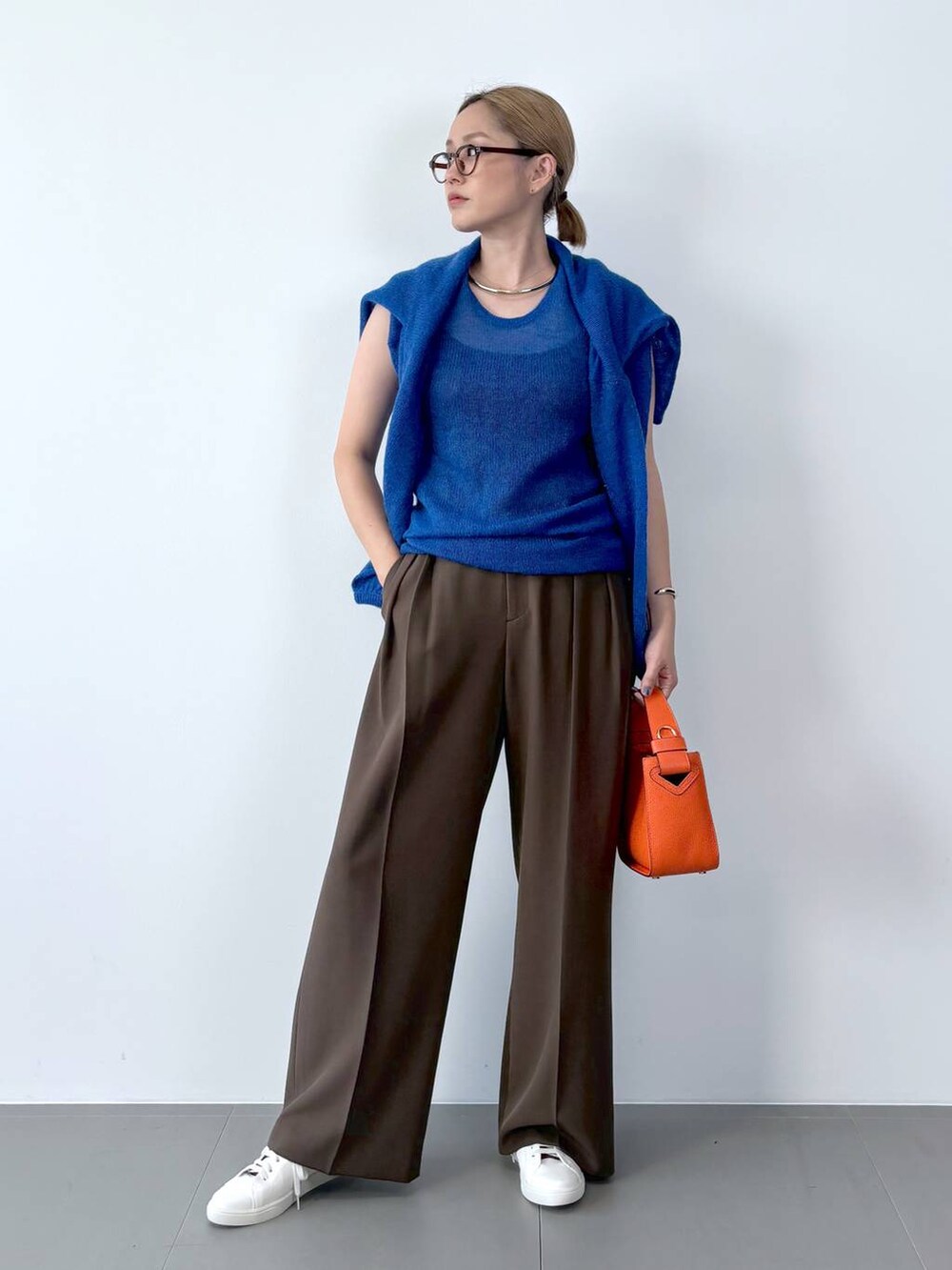 オレンジ系のハンドバッグ、ホワイト系のスニーカー、ブルー系のニット/セーターを着用したレディースの夏コーディネートの3枚目の写真