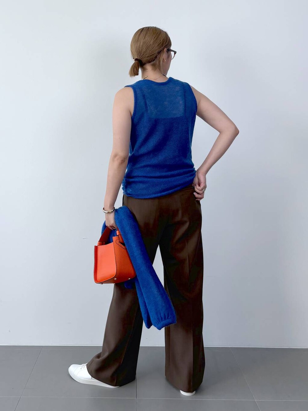 オレンジ系のハンドバッグ、ホワイト系のスニーカー、ブルー系のニット/セーターを着用したレディースの夏コーディネートの6枚目の写真