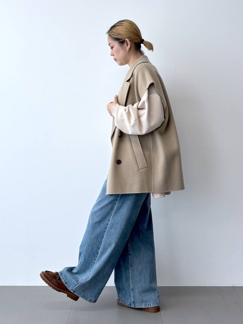 ブルー系のデニムパンツ、ベージュ系のベスト、ブラウン系のショルダーバッグを着用したレディースの秋コーディネートの4枚目の写真
