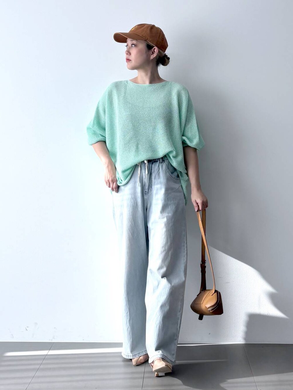 ブルー系のデニムパンツ、グリーン系のニット/セーター、ブラウン系のショルダーバッグを着用したレディースの春コーディネートの2枚目の写真