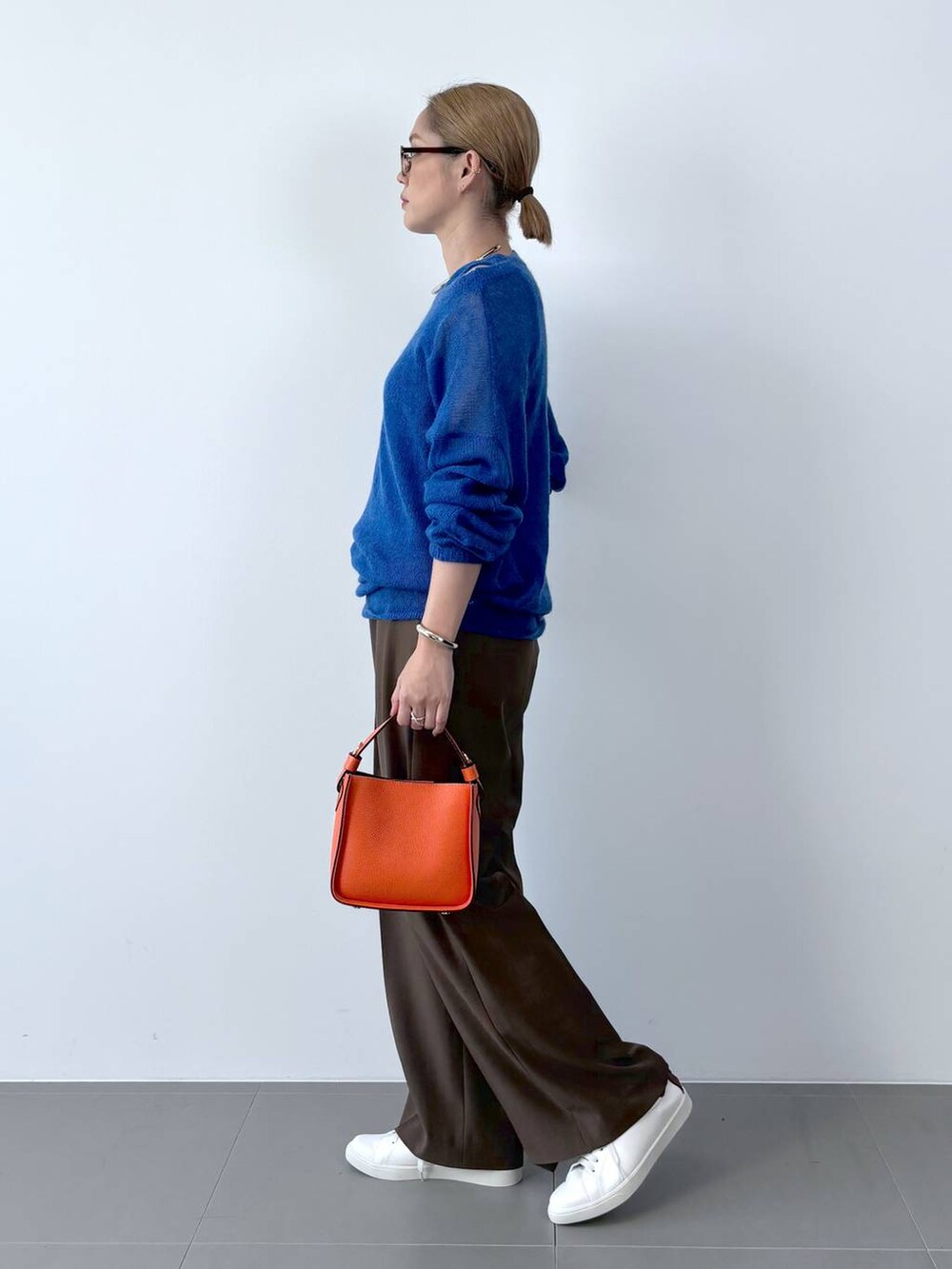 オレンジ系のハンドバッグ、ホワイト系のスニーカー、ブルー系のニット/セーターを着用したレディースの夏コーディネートの2枚目の写真