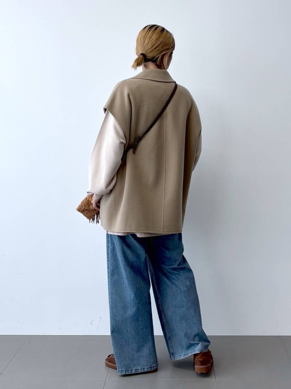 ブルー系のデニムパンツ、ベージュ系のベスト、ブラウン系のショルダーバッグを着用したレディースの秋コーディネートの5枚目の写真