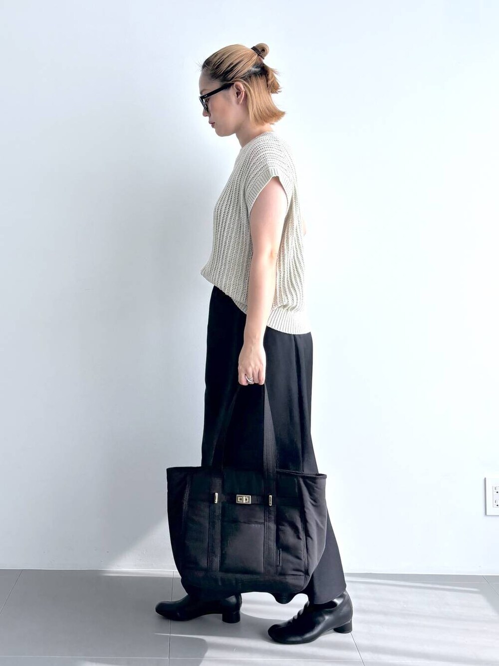 ブラック系のトートバッグ、ベージュ系のニット/セーター、ブラック系のスカートを着用したレディースの夏コーディネートの2枚目の写真
