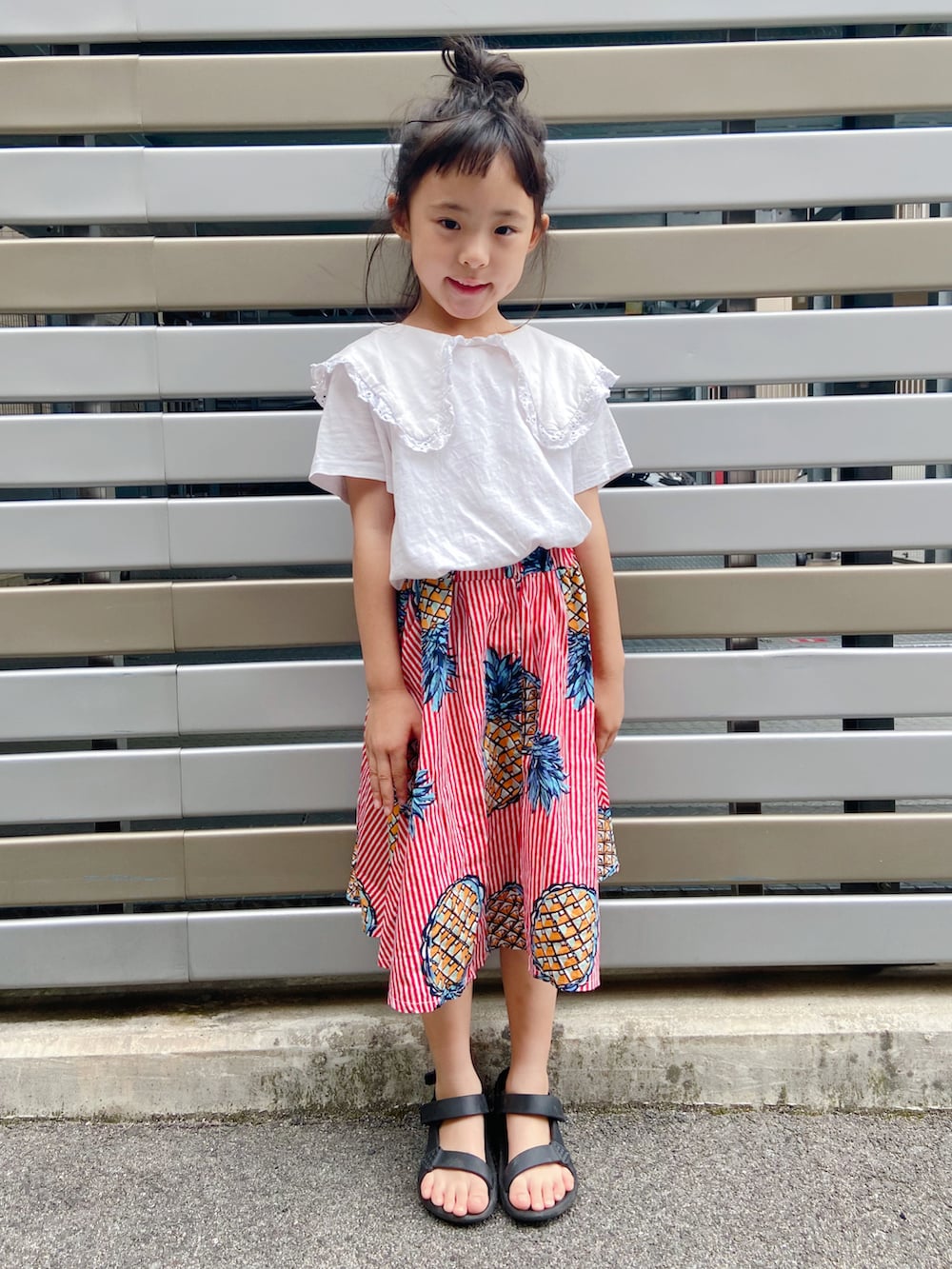 レッド系のスカート、ホワイト系のTシャツ/カットソー、ブラック系のサンダルを着用したキッズの夏コーディネートの2枚目の写真
