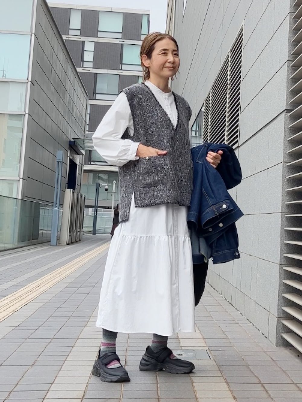 グレー系のベスト、ブルー系のデニムジャケット、ホワイト系のワンピース/ドレスを着用したレディースの春コーディネートの2枚目の写真