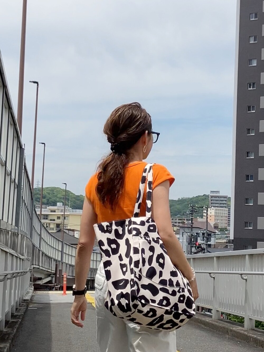 ベージュ系のトートバッグ、オレンジ系のTシャツ/カットソー、ホワイト系のパンツを着用したレディースの春コーディネートの3枚目の写真