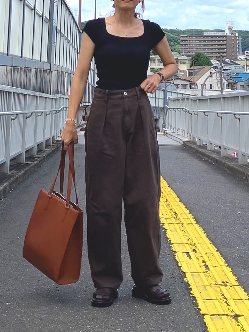 ブラック系のトップス、ブラウン系のデニムパンツ、ブラウン系のトートバッグを着用したレディースの夏コーディネートの2枚目の写真