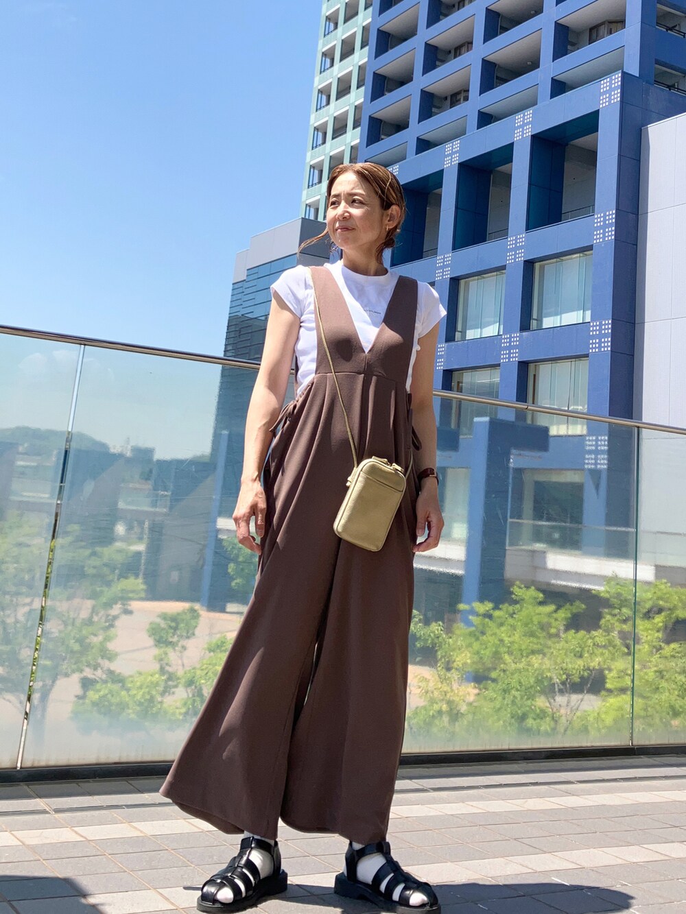 ブラウン系のサロペット/オーバーオール、ホワイト系のTシャツ/カットソー、ゴールド系のバッグを着用したレディースの春コーディネートの4枚目の写真