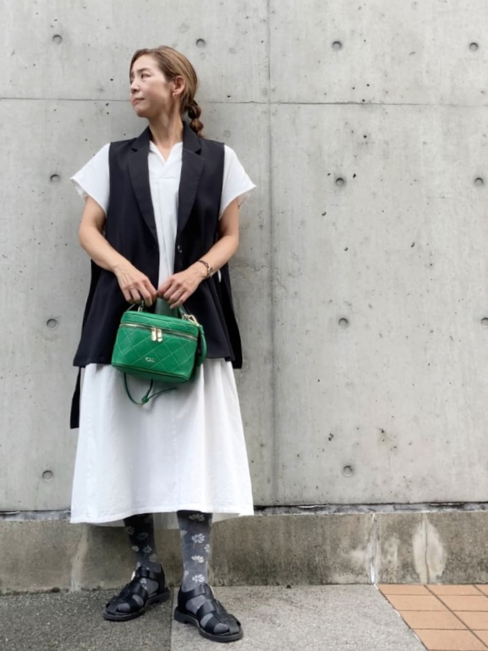 ブラック系のベスト、ホワイト系のワンピース、グリーン系のショルダーバッグを着用したレディースの夏コーディネートの2枚目の写真