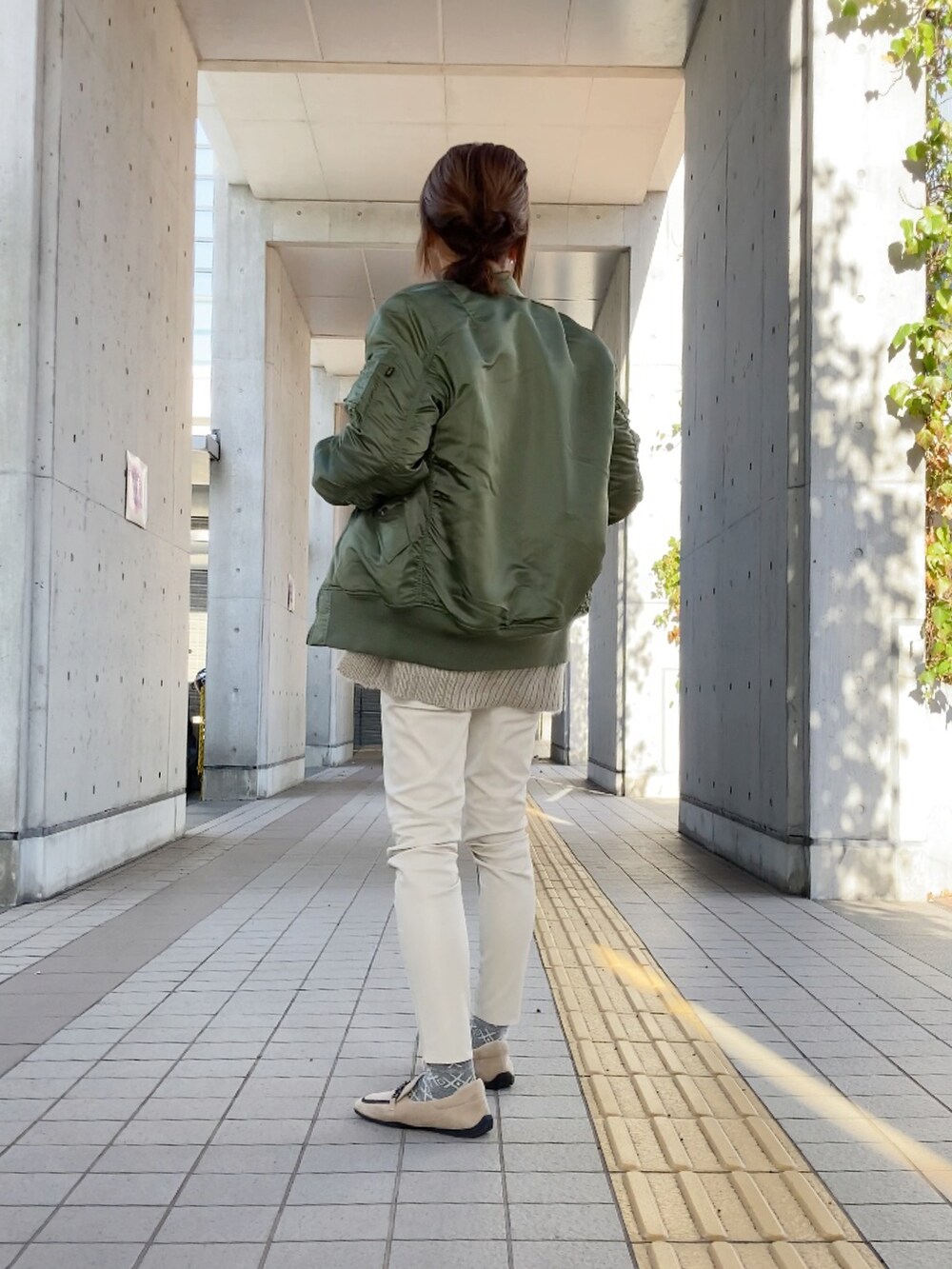 グリーン系のMA-1、ホワイト系のパンツ、ブラウン系のショルダーバッグを着用したレディースの冬コーディネートの2枚目の写真