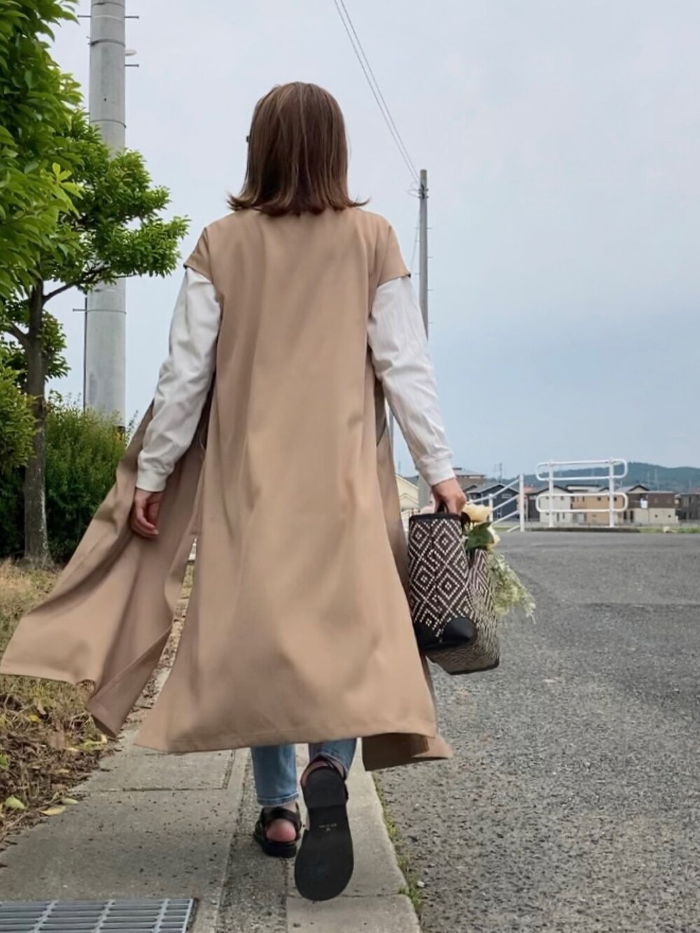 ベージュ系のワンピース、ブルー系のデニムパンツ、ブラック系のかごバッグを着用したレディースの春コーディネートの4枚目の写真