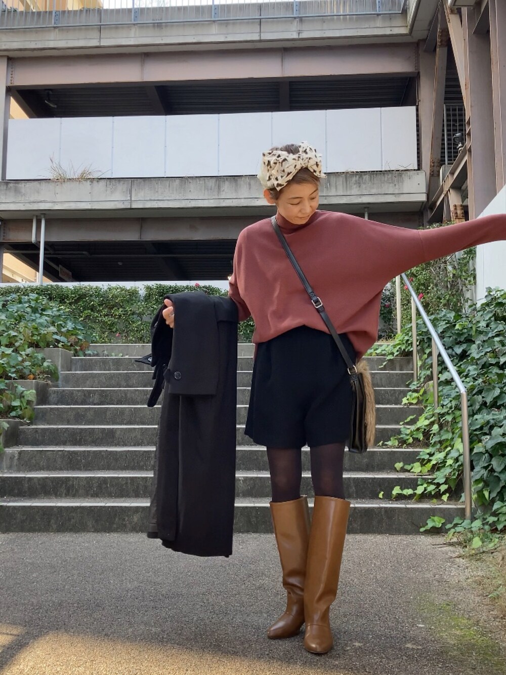 ブラック系のステンカラーコート、ブラウン系のニット/セーター、ブラック系のパンツを着用したレディースの冬コーディネートの3枚目の写真