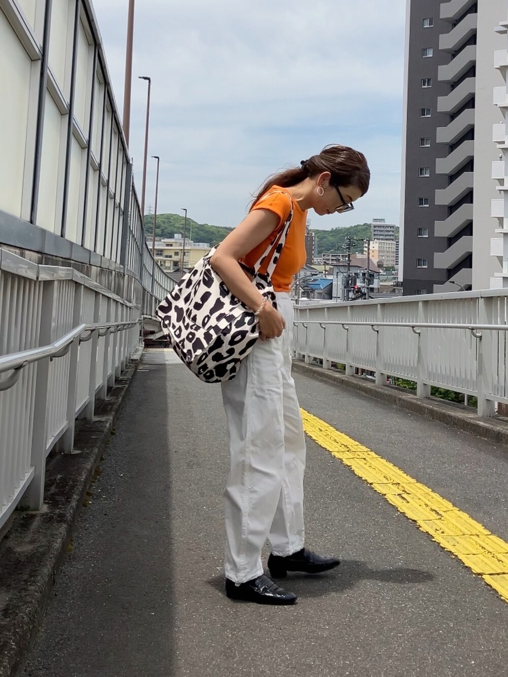 ベージュ系のトートバッグ、オレンジ系のTシャツ/カットソー、ホワイト系のパンツを着用したレディースの春コーディネートの4枚目の写真