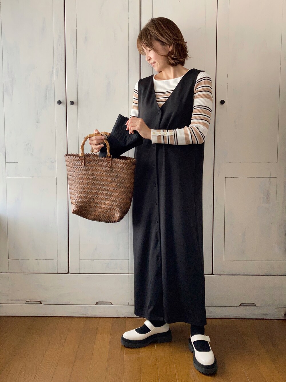 ブラック系のジャンパースカート、ホワイト系のニット/セーター、ブラウン系のかごバッグを着用したレディースの春コーディネートの2枚目の写真