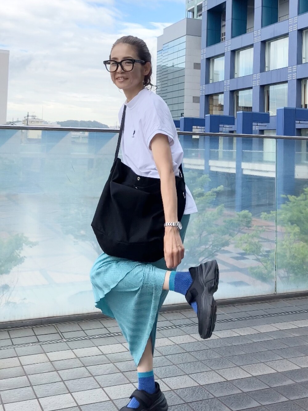 ブラック系のショルダーバッグ、ホワイト系のTシャツ/カットソー、ブルー系のスカートを着用したレディースの夏コーディネートの3枚目の写真