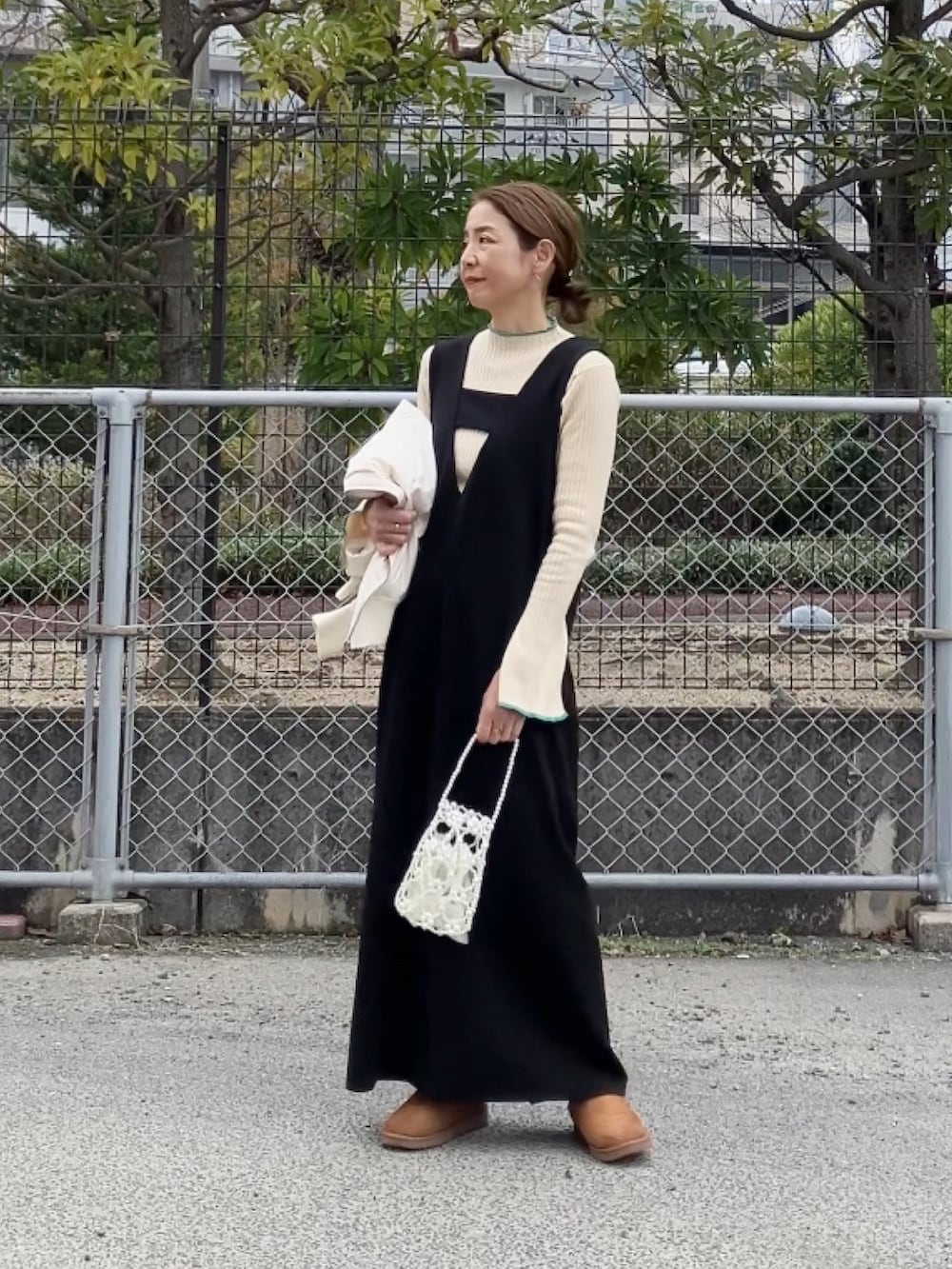 ブラック系のジャンパースカート、ホワイト系のハンドバッグ、イエロー系のサンダルを着用したレディースの冬コーディネートの4枚目の写真