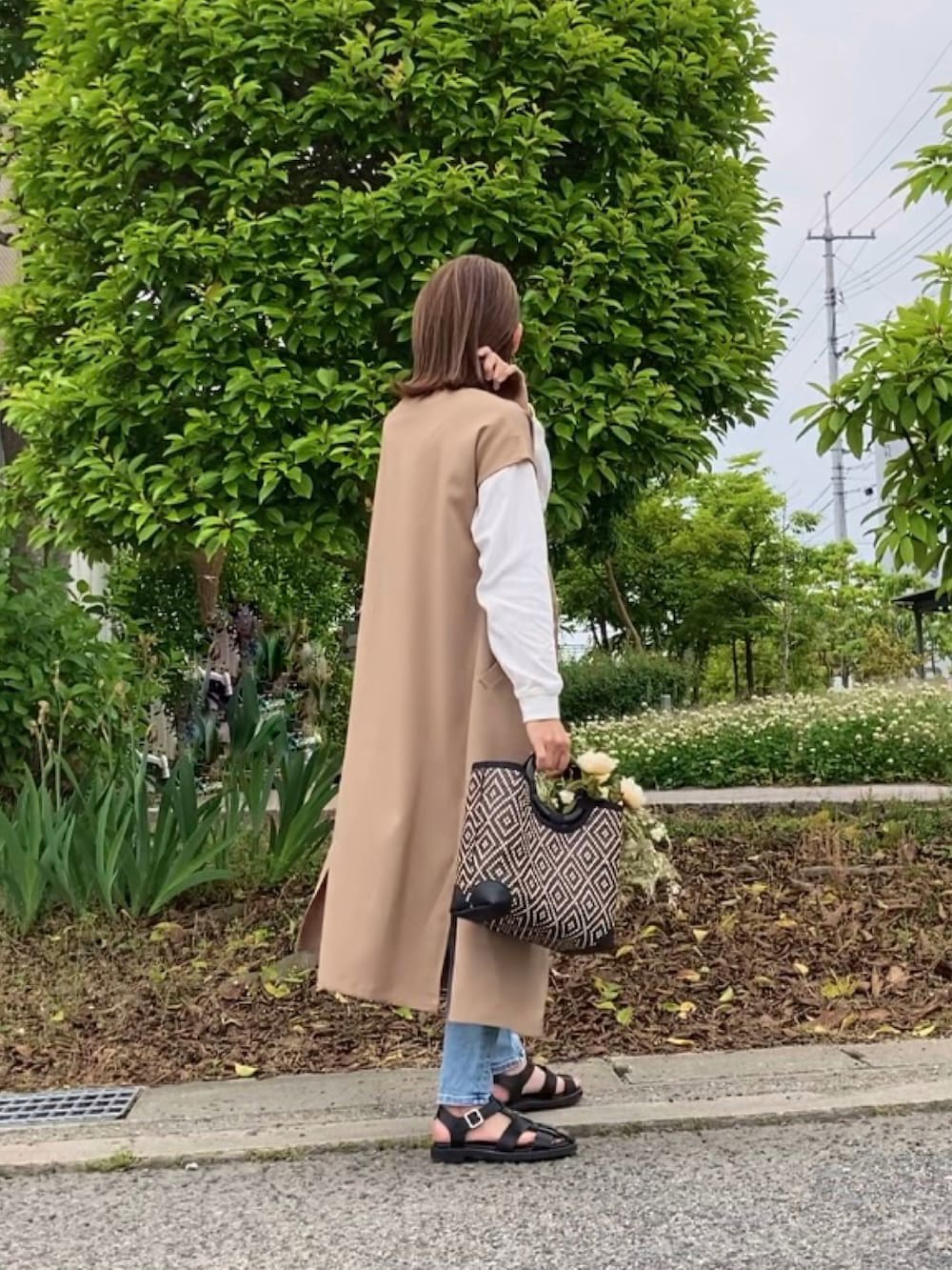 ベージュ系のワンピース、ブルー系のデニムパンツ、ブラック系のかごバッグを着用したレディースの春コーディネートの2枚目の写真