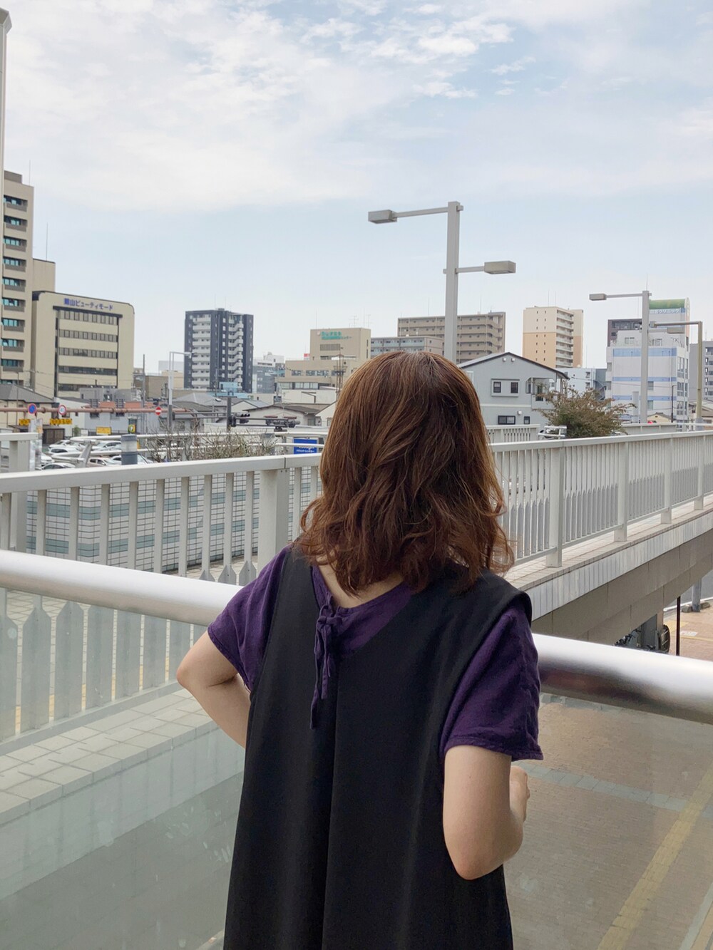 ブラック系のジャンパースカート、パープル系のワンピース、ブラウン系のバックパック/リュックを着用したレディースの春コーディネートの2枚目の写真