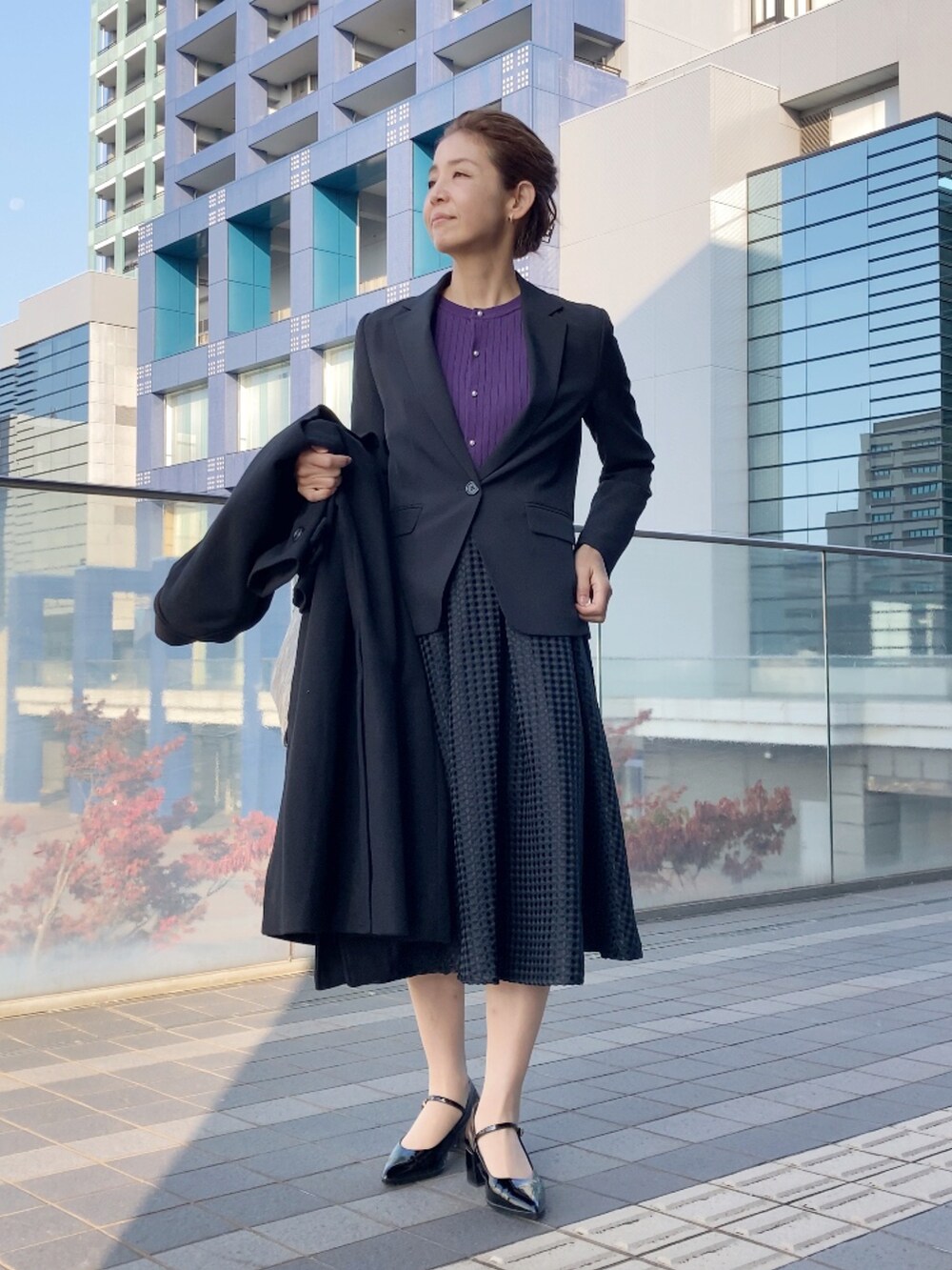 ブラック系のスーツセット、パープル系のカーディガン/ボレロ、ブラック系のスカートを着用したレディースの秋コーディネートの2枚目の写真