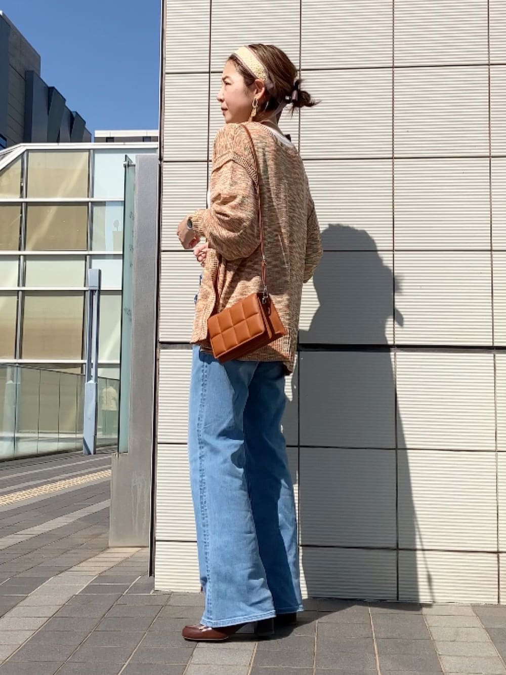 オレンジ系のカーディガン/ボレロ、ブラウン系のクラッチバッグ、ブルー系のデニムパンツを着用したレディースの春コーディネートの2枚目の写真