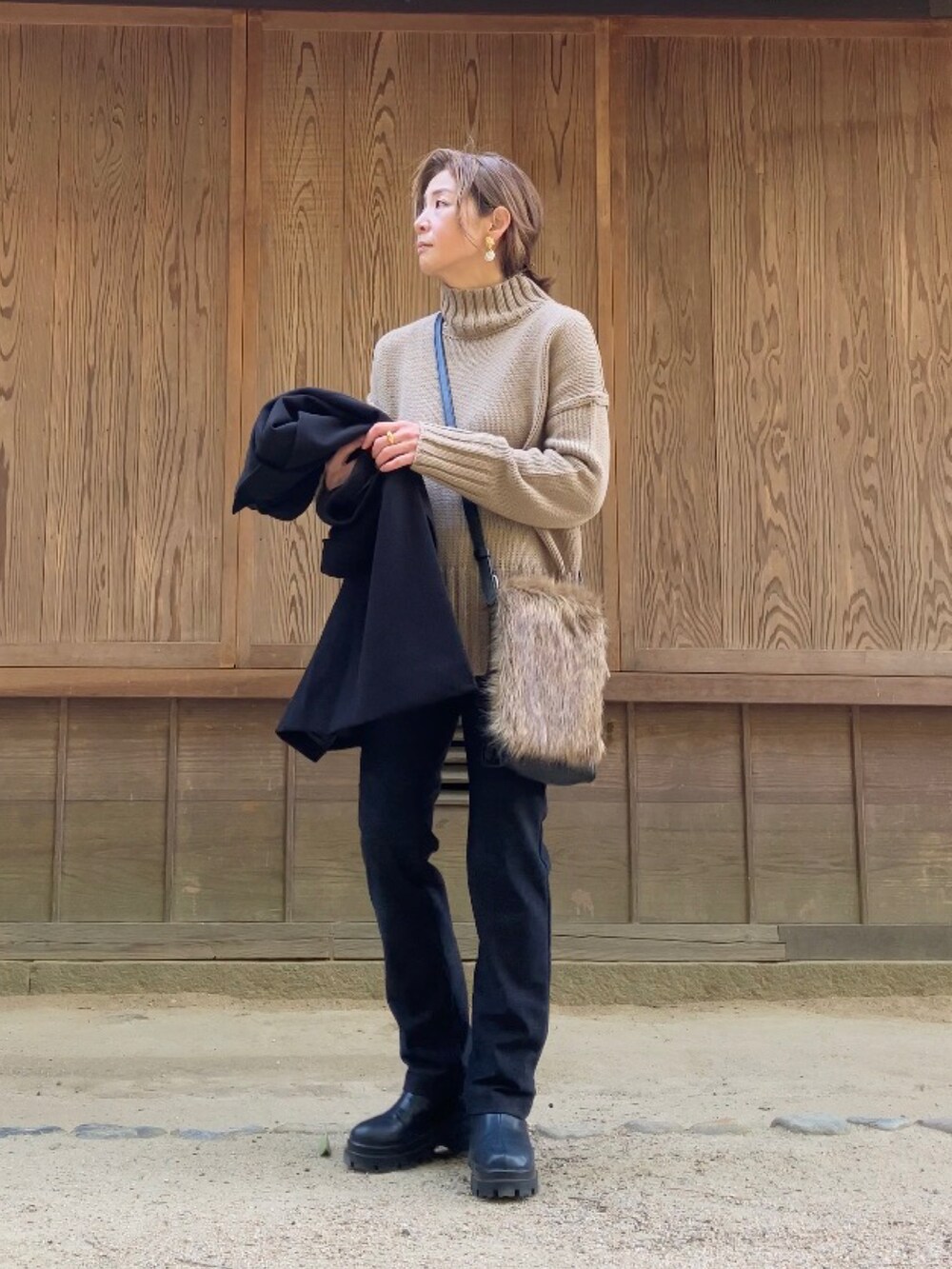 ブラック系のパンツ、ブラック系のステンカラーコート、ベージュ系のニット/セーターを着用したレディースの冬コーディネートの2枚目の写真