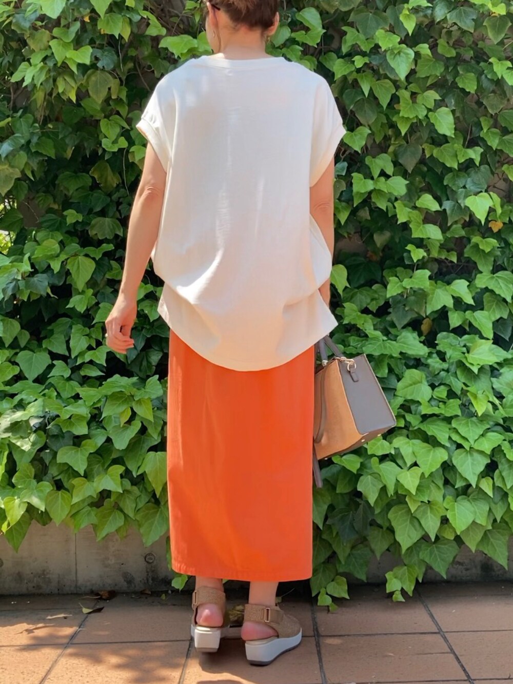 ホワイト系のTシャツ/カットソー、オレンジ系のスカート、グレー系のハンドバッグを着用したレディースの春コーディネートの3枚目の写真