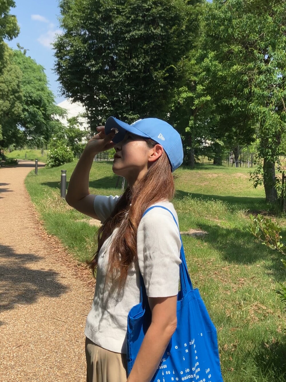 ベージュ系のパンツ、ホワイト系のポロシャツ、ブルー系のトートバッグを着用したレディースの夏コーディネートの2枚目の写真