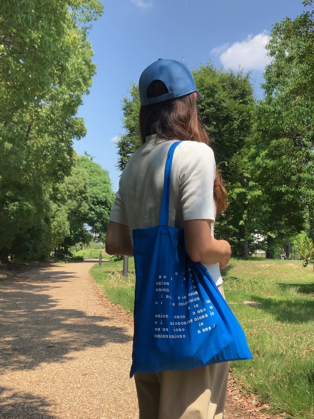 ベージュ系のパンツ、ホワイト系のポロシャツ、ブルー系のトートバッグを着用したレディースの夏コーディネートの5枚目の写真