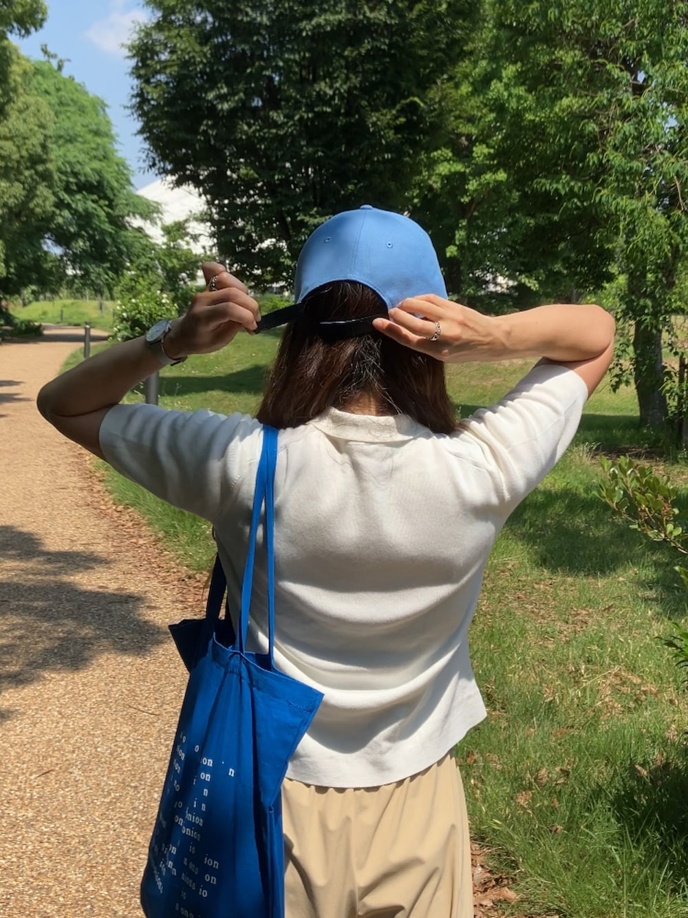 ベージュ系のパンツ、ホワイト系のポロシャツ、ブルー系のトートバッグを着用したレディースの夏コーディネートの3枚目の写真