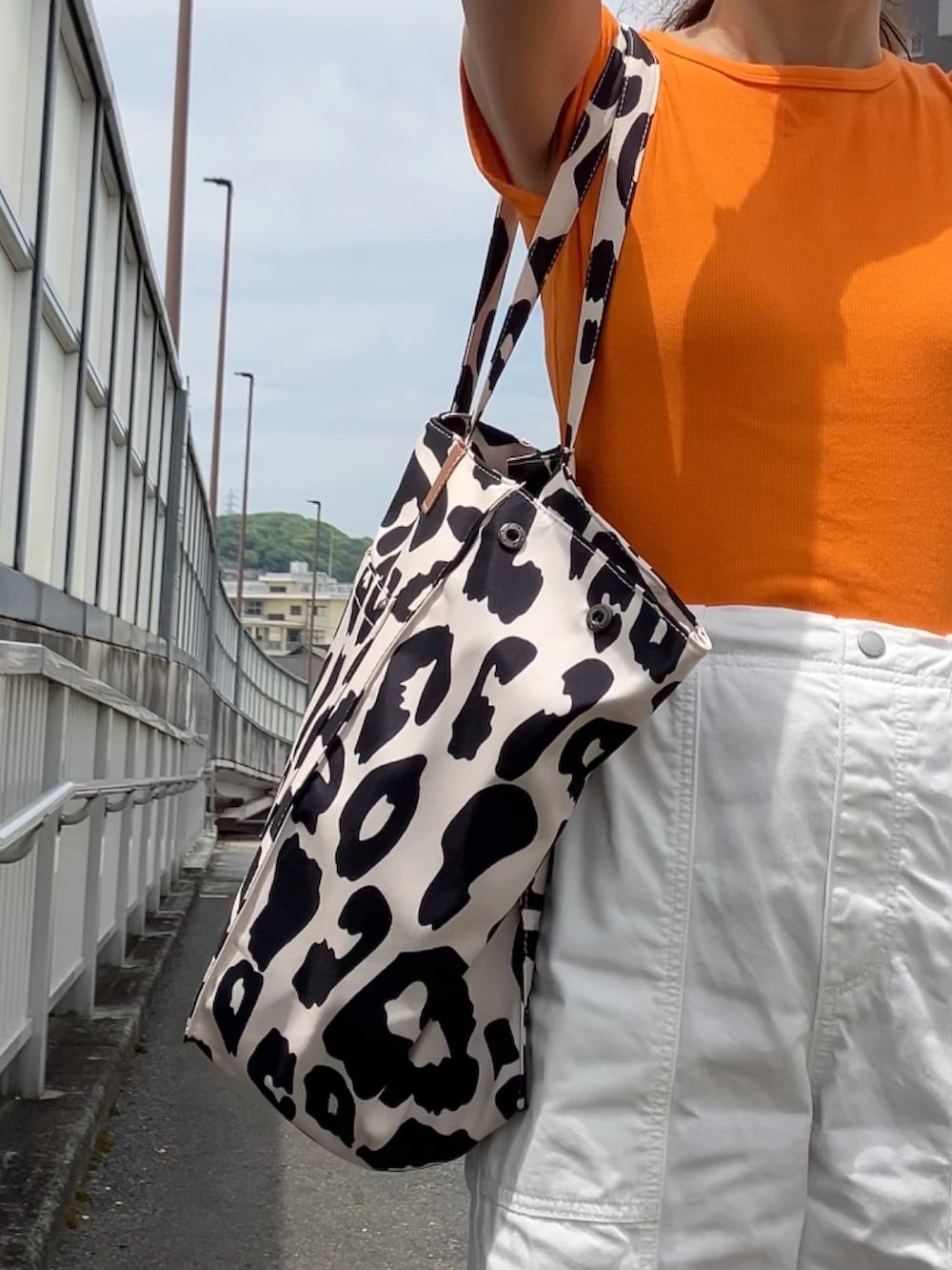 ベージュ系のトートバッグ、オレンジ系のTシャツ/カットソー、ホワイト系のパンツを着用したレディースの春コーディネートの2枚目の写真