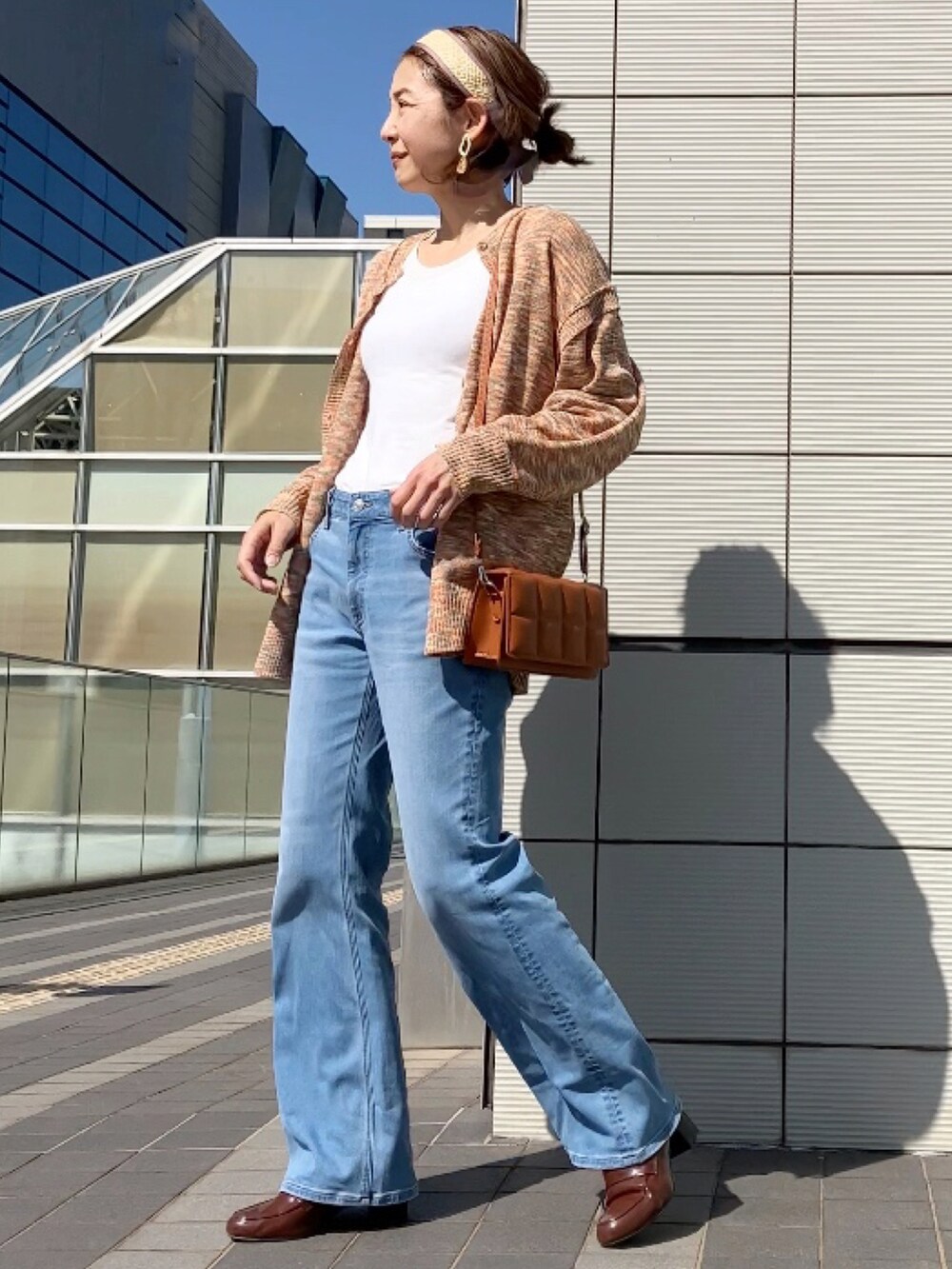 オレンジ系のカーディガン/ボレロ、ブラウン系のクラッチバッグ、ブルー系のデニムパンツを着用したレディースの春コーディネートの5枚目の写真