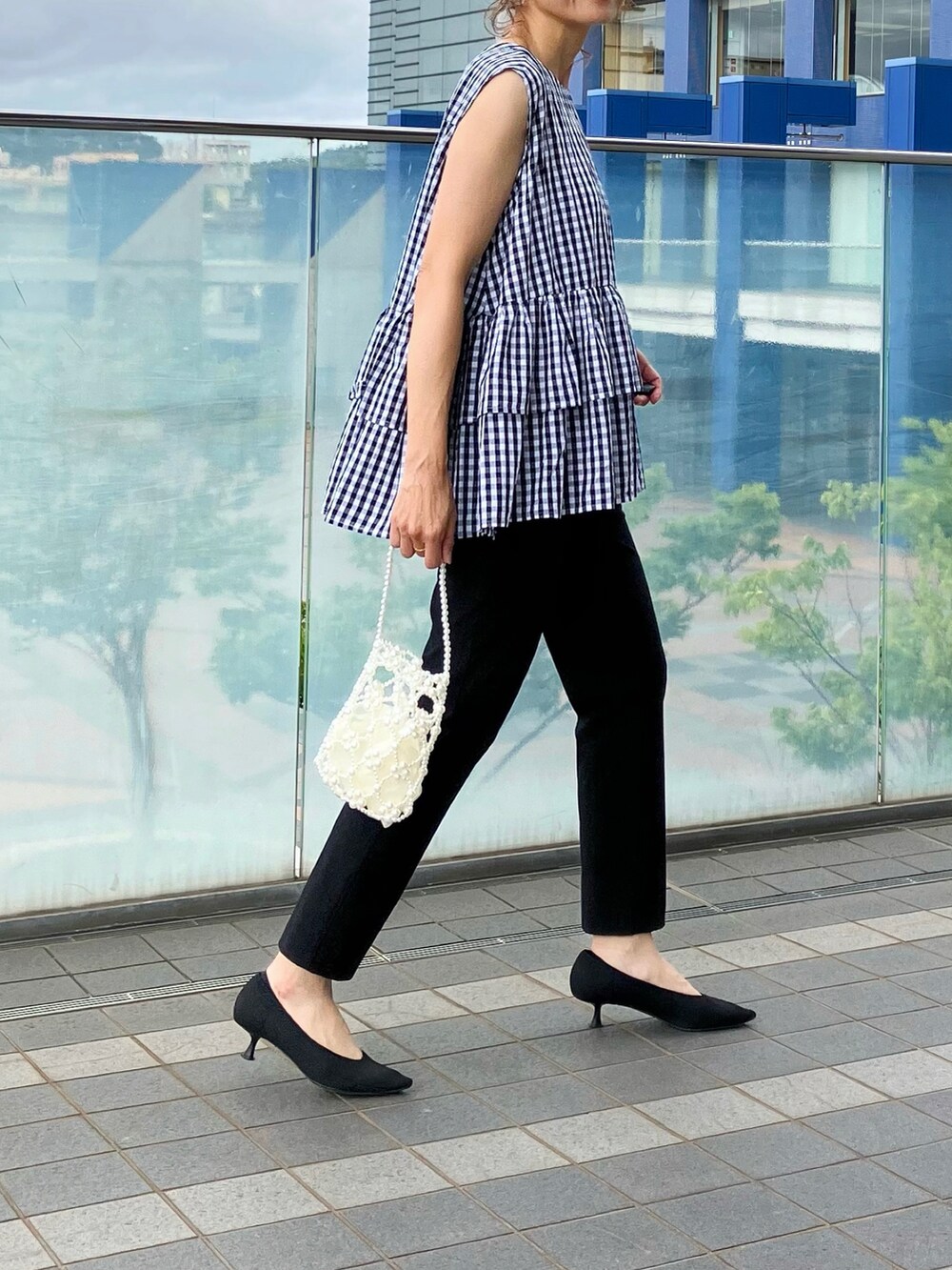 ブラック系のトップス、ホワイト系のハンドバッグ、ブラック系のパンツを着用したレディースの夏コーディネートの2枚目の写真