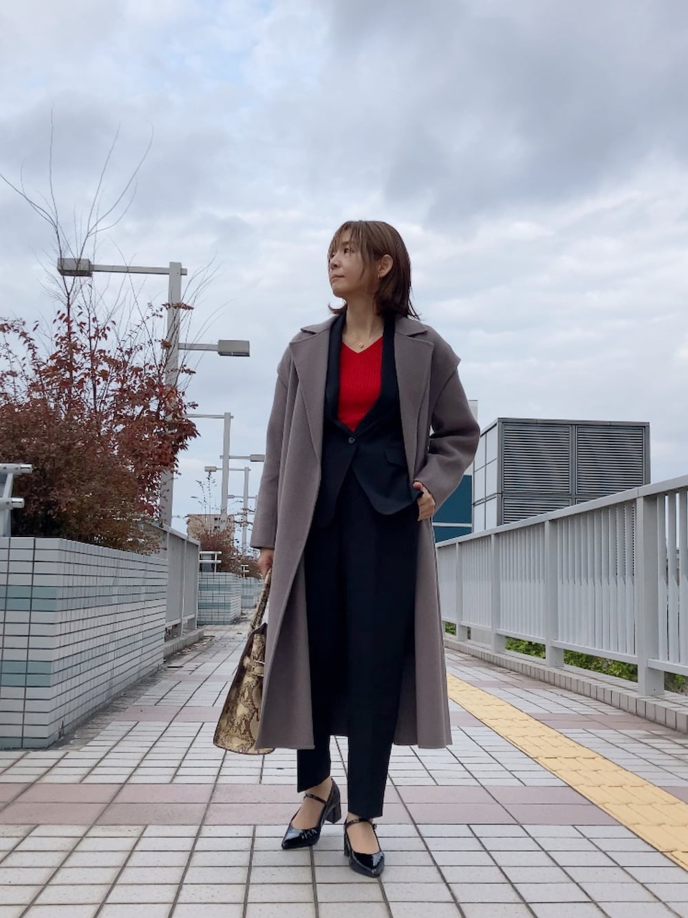 ブラウン系のチェスターコート、ブラック系のスーツセット、ブラック系のシューズを着用したレディースの秋コーディネートの3枚目の写真