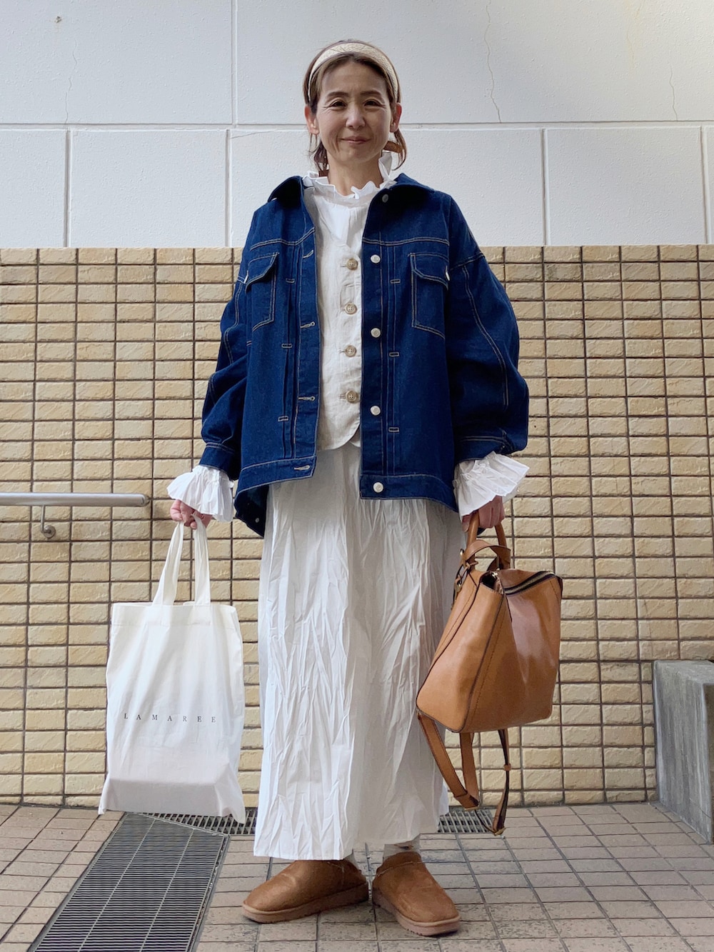 ベージュ系のベスト、ブルー系のデニムジャケット、ホワイト系のワンピースを着用したレディースの春コーディネートの5枚目の写真