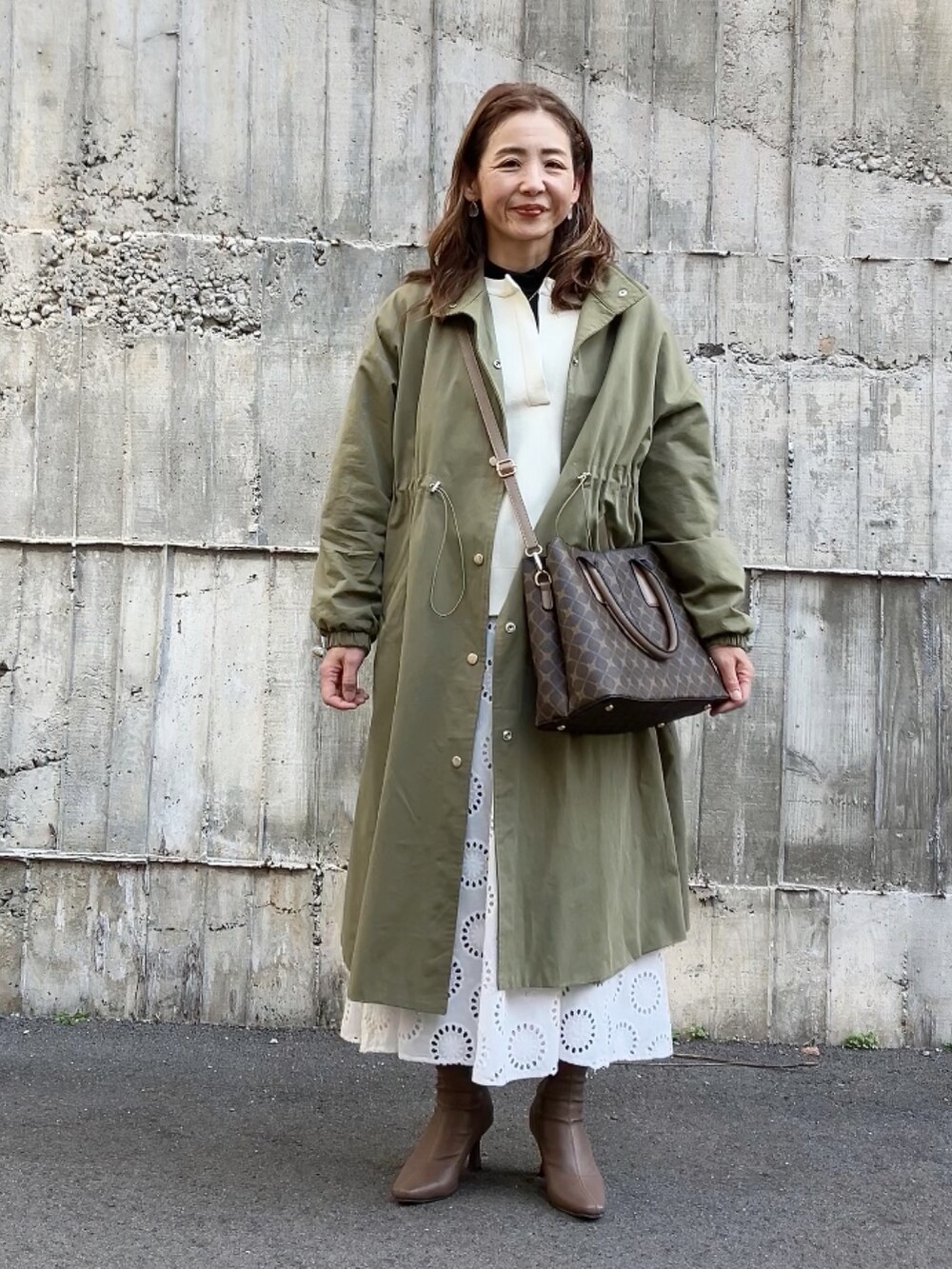 グリーン系のステンカラーコート、ブラウン系のハンドバッグ、ホワイト系のワンピース/ドレスを着用したレディースの冬コーディネートの5枚目の写真