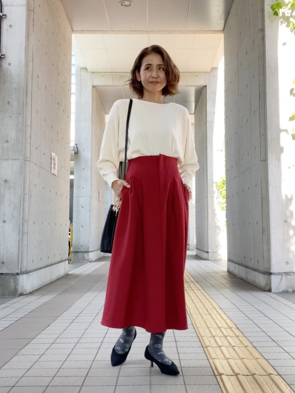 ホワイト系のニット/セーター、レッド系のスカート、ブラック系のハンドバッグを着用したレディースの秋コーディネートの4枚目の写真
